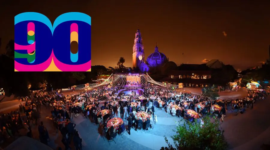 A vibrant nighttime scene of a large, elegant outdoor gala event with string lights and festive decorations, set in front of a beautifully lit historic tower and dome structure. A colorful "90" logo in bold, layered colors appears in the top left corner.