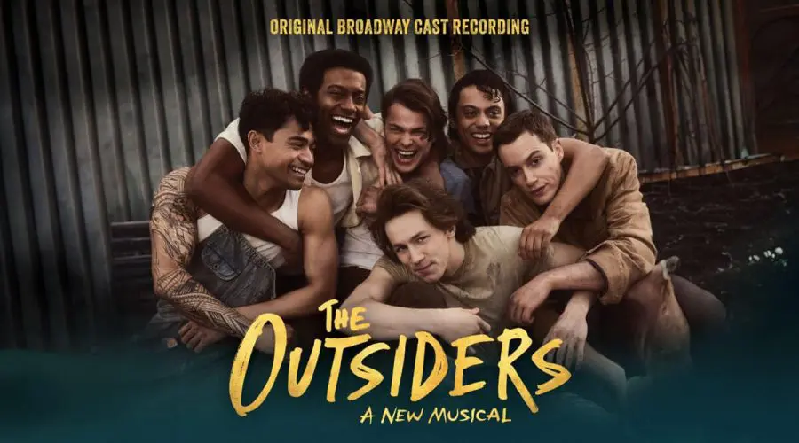 The cast of The Outsiders: A New Musical smiles and embraces each other in front of a corrugated metal backdrop. The text "Original Broadway Cast Recording" appears above them, and the show's title "The Outsiders: A New Musical" is displayed at the bottom.