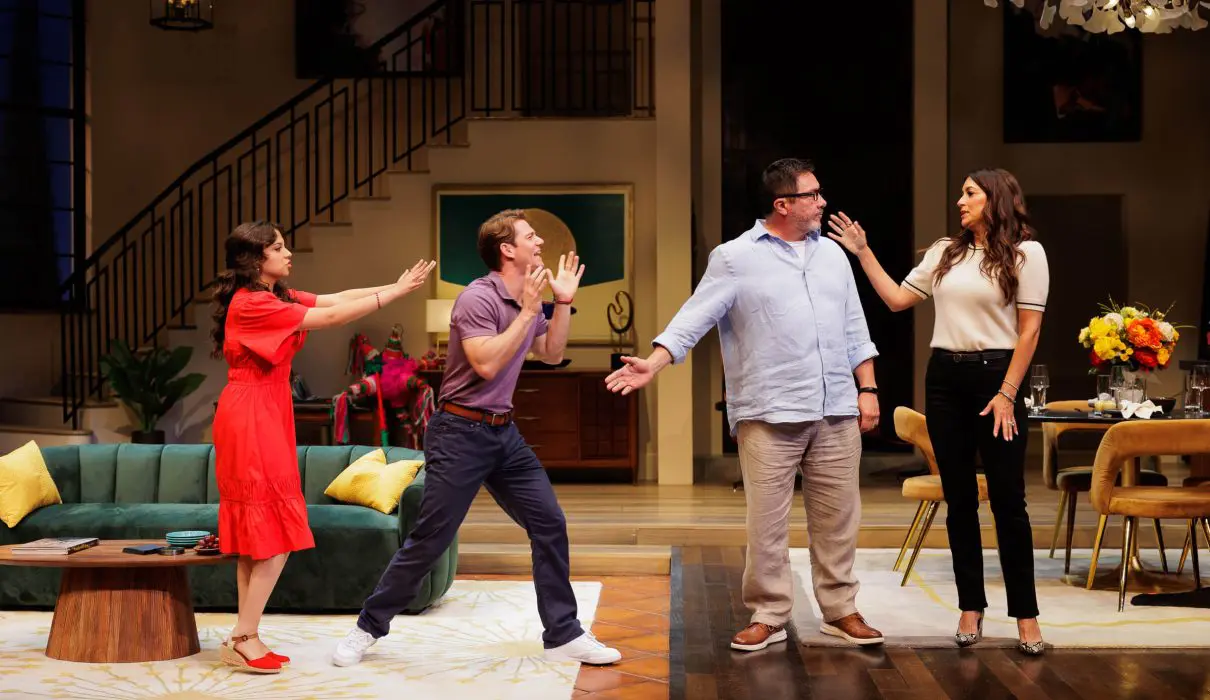 Scene from the 2025 play One of the Good Ones featuring Cree as Yoli, Nico Greetham as Marcos, Benito Martinez as Enrique, and Angelique Cabral as Ilana. All four characters are animated and mid-gesture in what appears to be a heated or comedic exchange in a stylish living room set. A broken piñata lies in the background near a green couch and modern decor. Photo by Rich Soublet II.