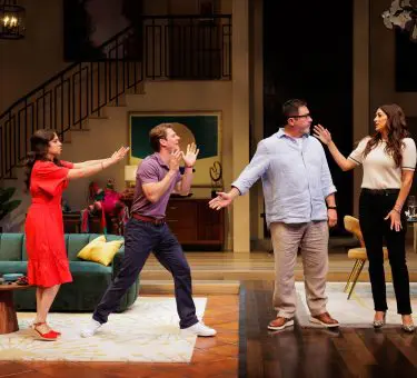 Scene from the 2025 play One of the Good Ones featuring Cree as Yoli, Nico Greetham as Marcos, Benito Martinez as Enrique, and Angelique Cabral as Ilana. All four characters are animated and mid-gesture in what appears to be a heated or comedic exchange in a stylish living room set. A broken piñata lies in the background near a green couch and modern decor. Photo by Rich Soublet II.