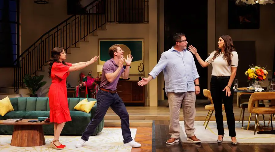 Scene from the 2025 play One of the Good Ones featuring Cree as Yoli, Nico Greetham as Marcos, Benito Martinez as Enrique, and Angelique Cabral as Ilana. All four characters are animated and mid-gesture in what appears to be a heated or comedic exchange in a stylish living room set. A broken piñata lies in the background near a green couch and modern decor. Photo by Rich Soublet II.