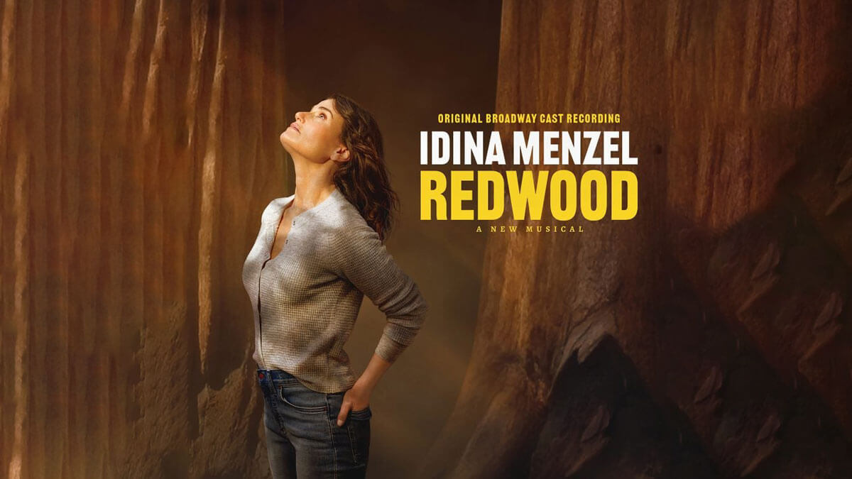 Promotional image for the original Broadway cast recording of Redwood, a new musical starring Idina Menzel. Idina stands among towering redwood trees, gazing upward with a serene expression, wearing a casual gray shirt and jeans. The title text "IDINA MENZEL REDWOOD" appears boldly in white and yellow on the right side.