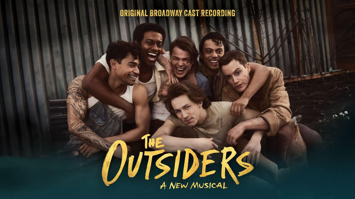 The cast of The Outsiders: A New Musical smiles and embraces each other in front of a corrugated metal backdrop. The text "Original Broadway Cast Recording" appears above them, and the show's title "The Outsiders: A New Musical" is displayed at the bottom.